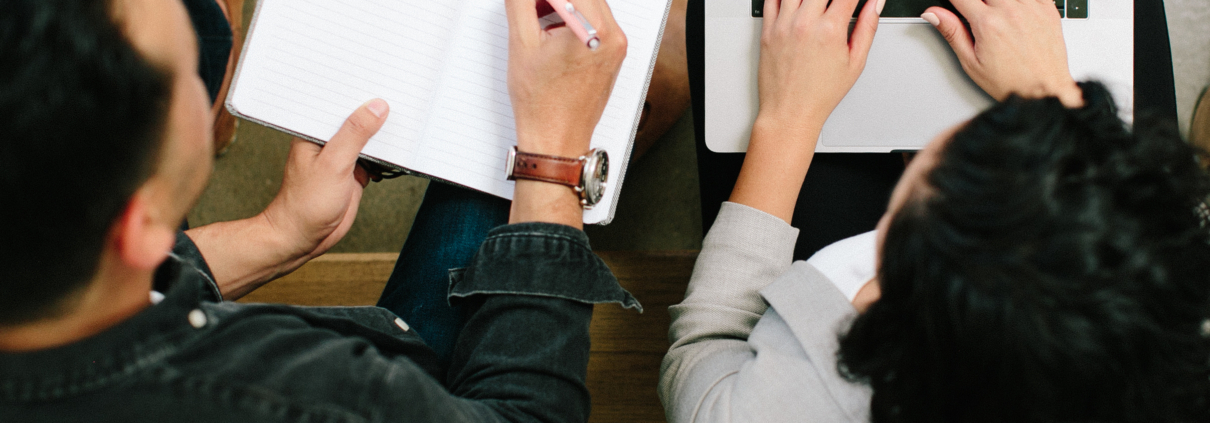 two people. One is typing on a computer. One is holding a paper.