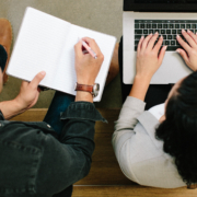 two people. One is typing on a computer. One is holding a paper.